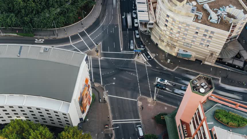 Cars and people walk and drive through a large city intersection