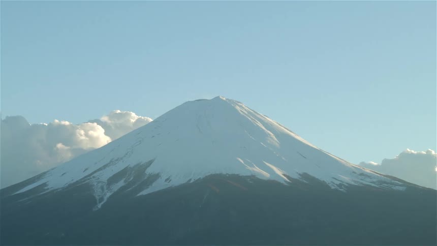 Clouds float near a snow capped mountain peak
