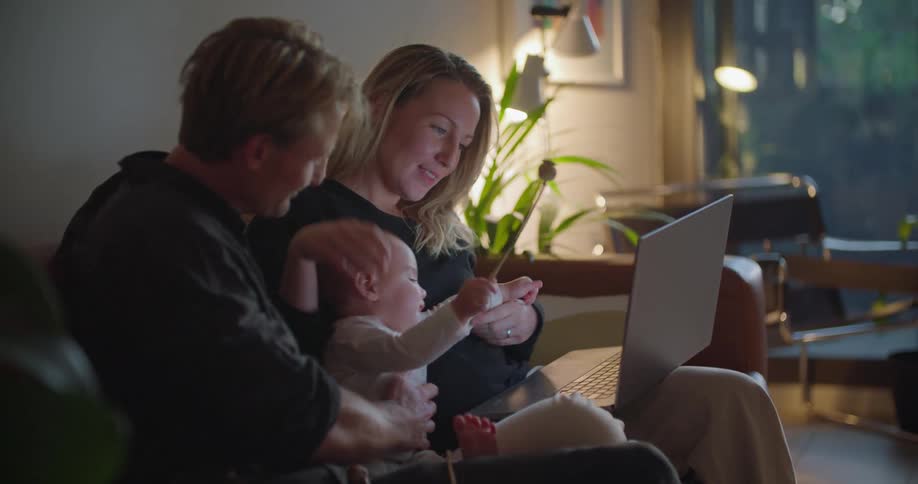 Parents and child sit on couch as mother uses laptop