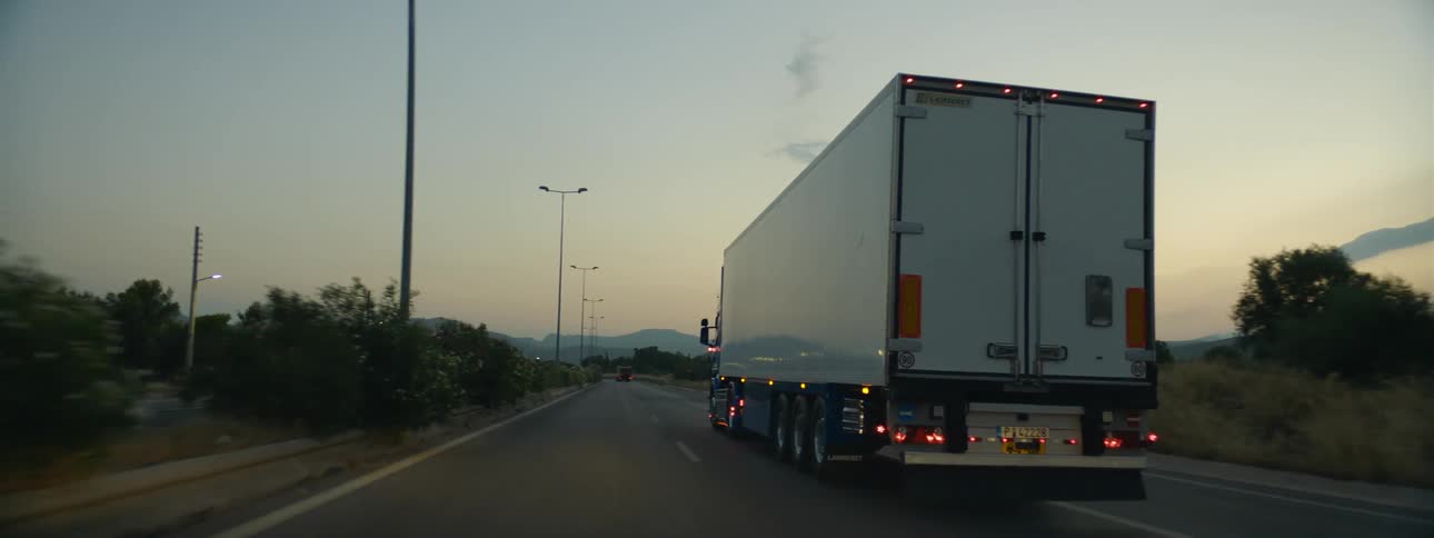 A semi truck travels on a highway at dusk