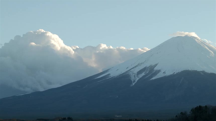 Smoke clouds build behind a mountain