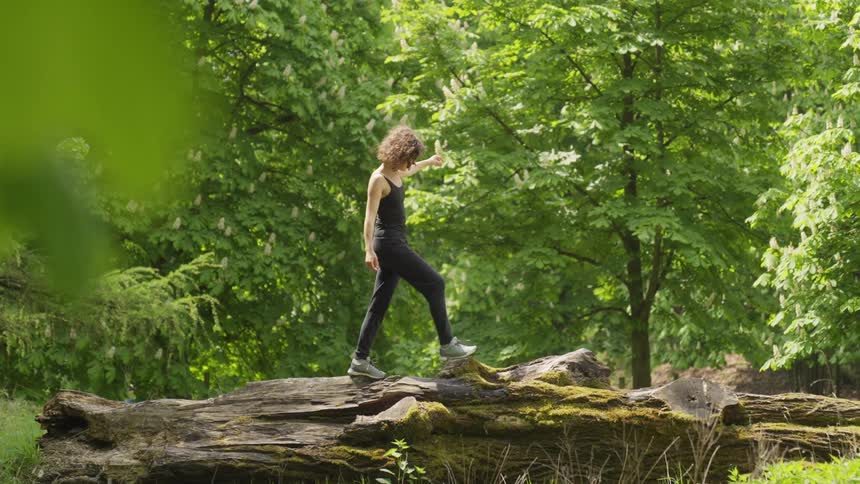 The sun shines upon a woman walking across a log in the woods
