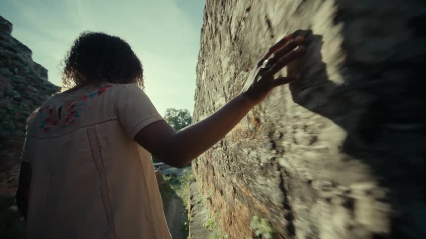 A woman runs her fingers along the side of a canyon and spins around