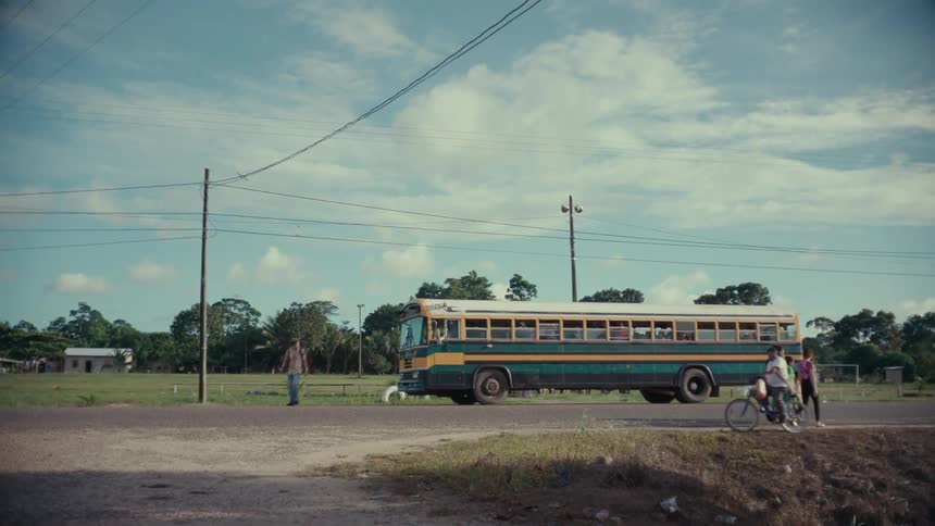 A school bus drops off a child while other people walk around and ride bikes