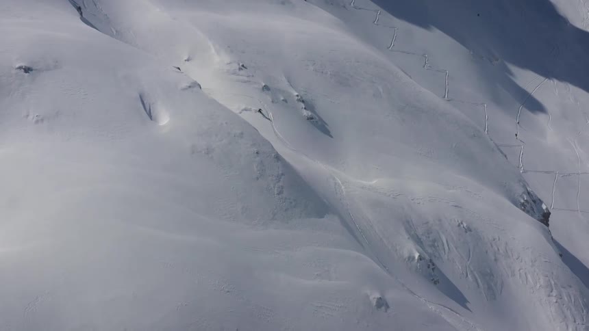 An aerial view of a skier speeding down a snowy mountainside