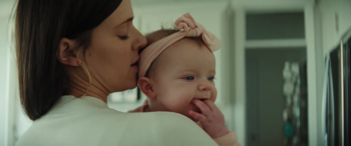 A woman kisses and rocks a baby girl in her arms while standing indoors during the day