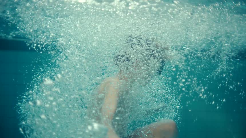 A young boy jumping into a swimming pool while wearing goggles