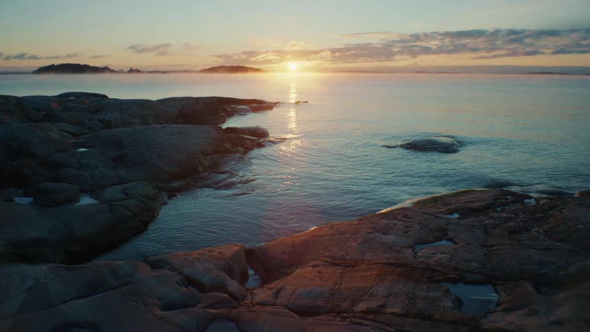Water ripples and gently splashes against the rocks as the sun sets on the horizon