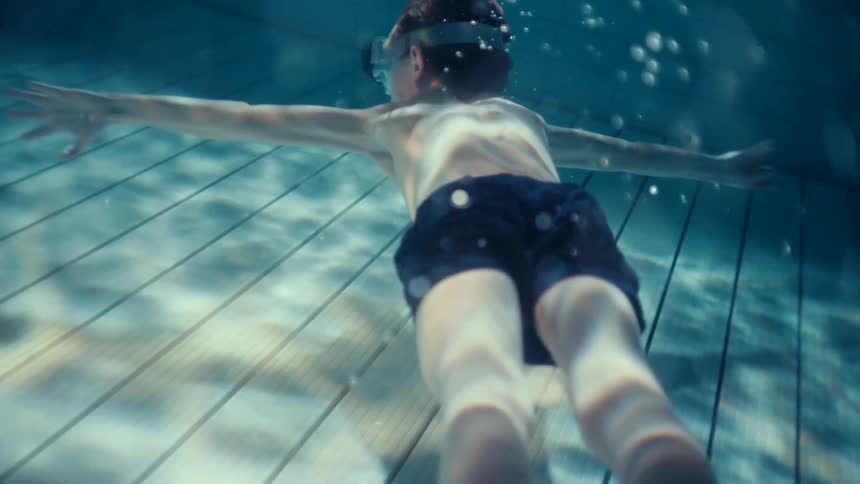A young boy with goggles swimming underwater in a pool