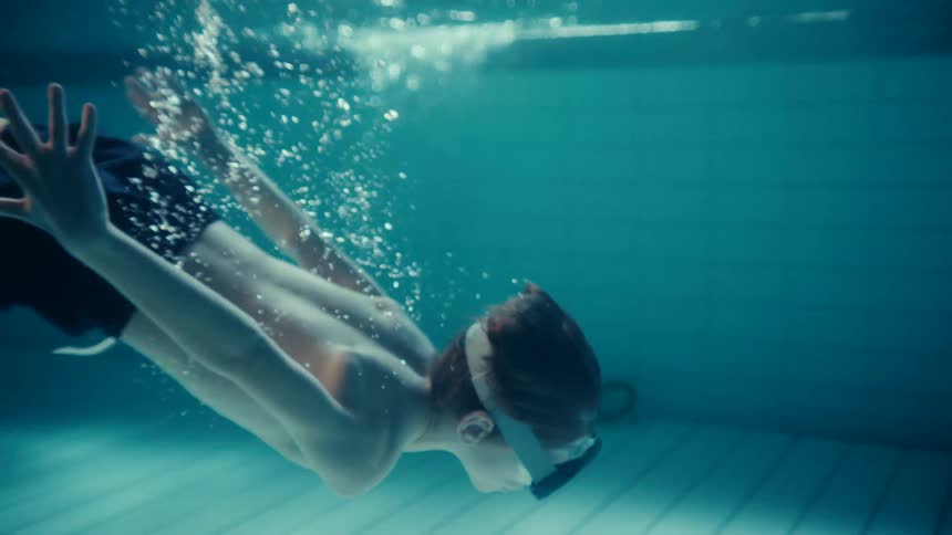 Boy wearing goggles swims underwater in swimming pool
