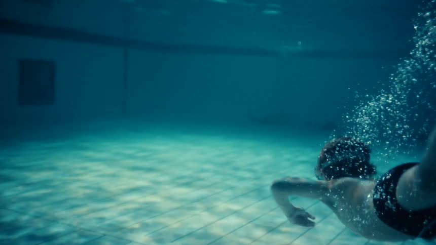 A little boy is wearing swimming goggles as he swims underwater in a pool