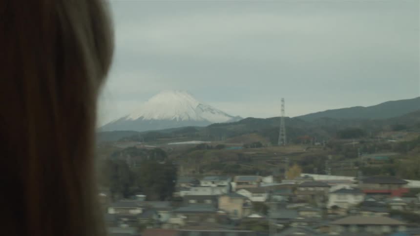 A woman is traveling sitting and looking out a window passing by