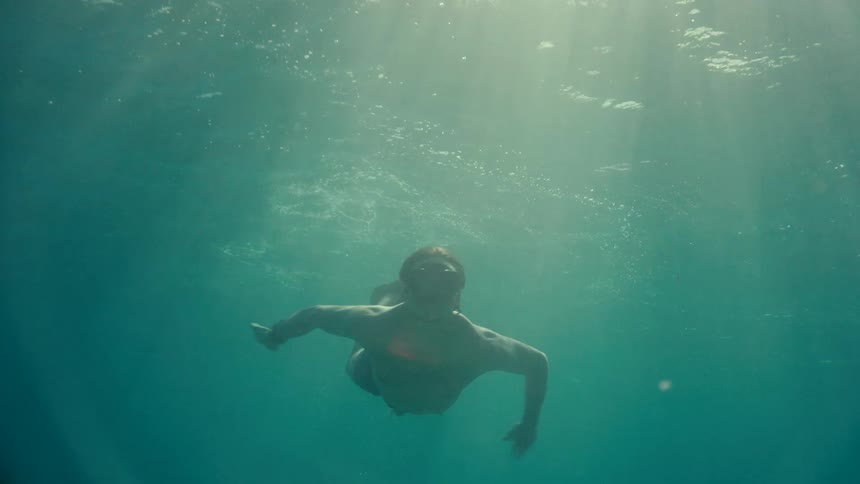 Man swims underwater using flippers as sun shines down from overhead
