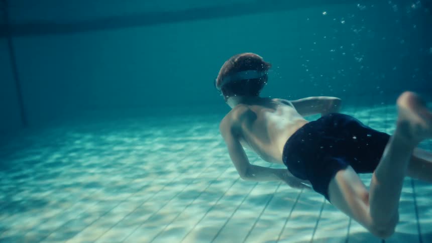 A little boy is wearing swimming goggles as he swims underwater in a swimming pool