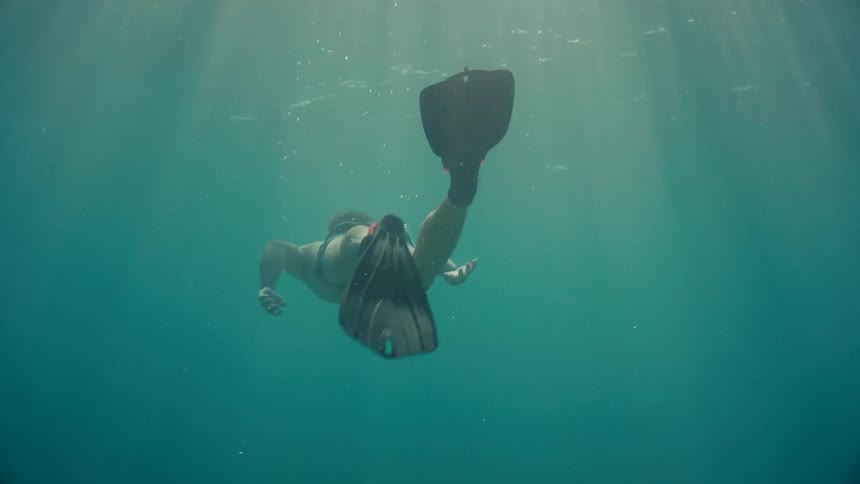 Swimmerwearing flippers heads to surface as sun shines rays through the water