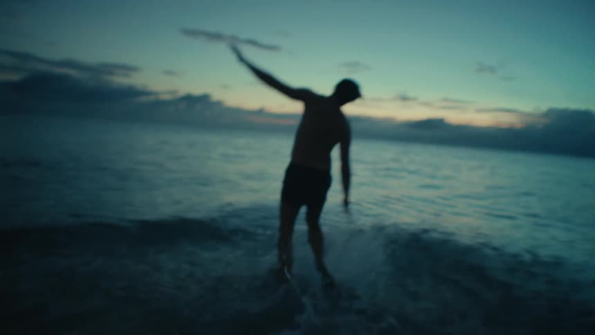 Youth runs across beach toward red tinted horizon and jumps in to the water