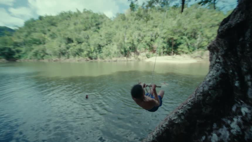 A boy swings from a tree over a river and jumps in