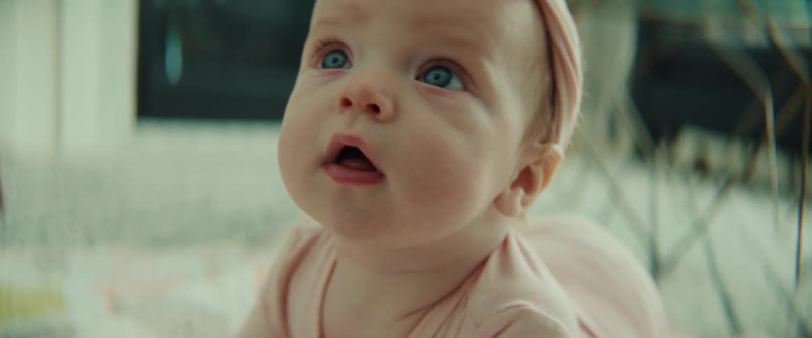 A baby looks around at her surroundings and smiles while lying on the floor indoors