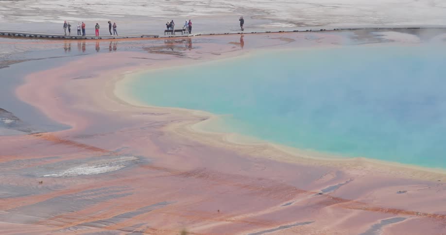 People move along edge of steaming colorful hot spring