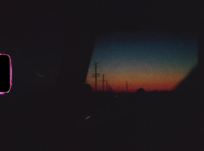 Someone is filming sunrise or sunset in a car driving down a desolate road