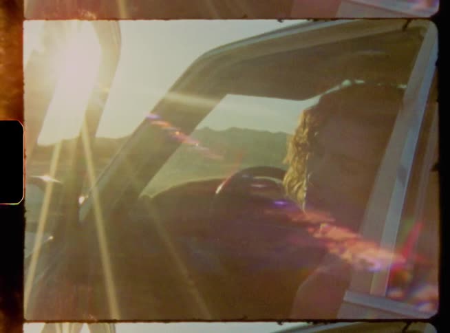 Redheaded woman sits in car with open door as bright sun shines from over the mountains