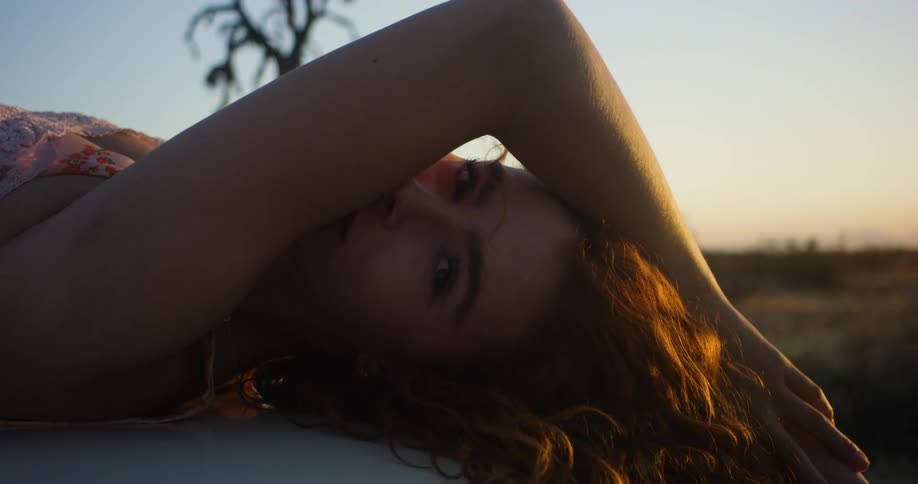 A woman is laying on a car and posing for a portrait