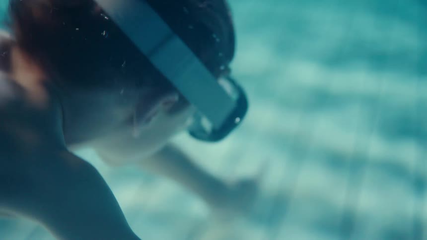 A view from underwater when a boy jumps into a swimming pool creating a storm of bubbles and looks around while wearing goggles