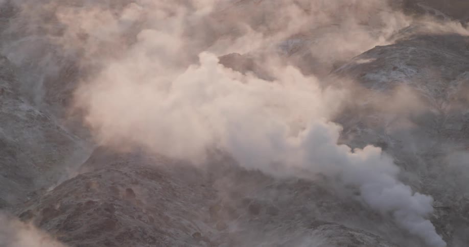 Smoke rises from surface and floats over ground in hilly terrain