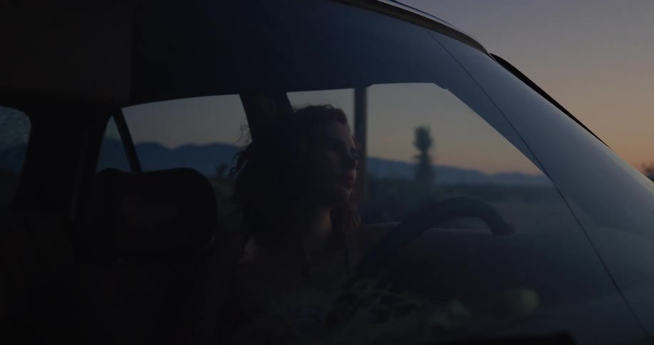 A woman is driving a car while the sun is setting