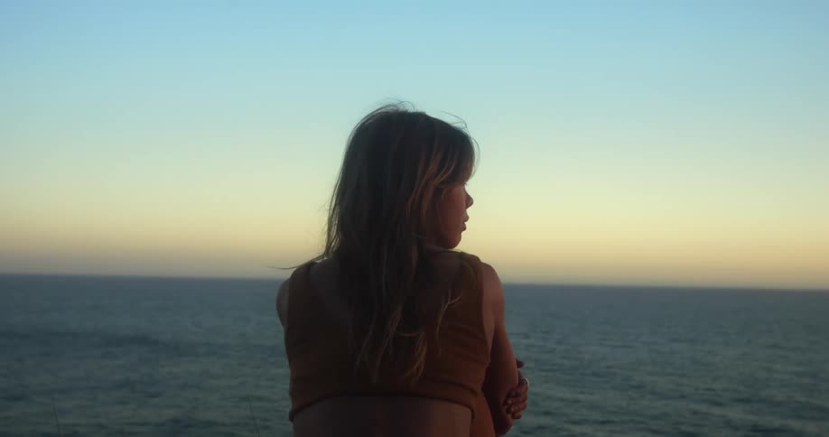 A woman is standing outdoors near a body of water at dusk