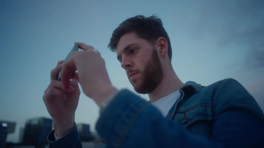 Man stands with city skyscrapers as a backdrop as he takes pictures with his smartphone