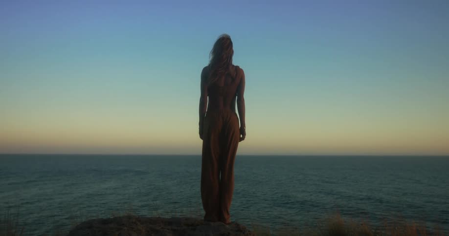 A woman standing on the coast looks out over the ocean in the evening
