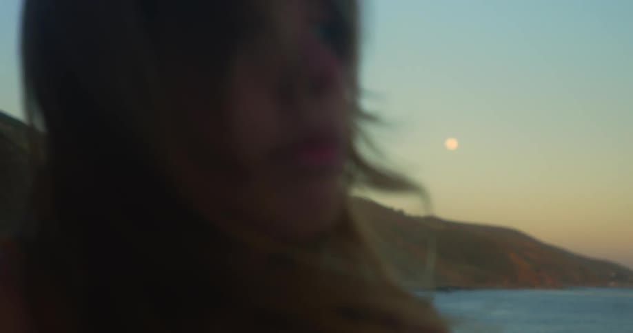 A woman is standing outdoors at the beach during dusk