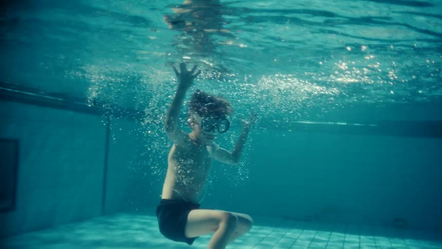 A boy dives into a swimming pool and remains underwater