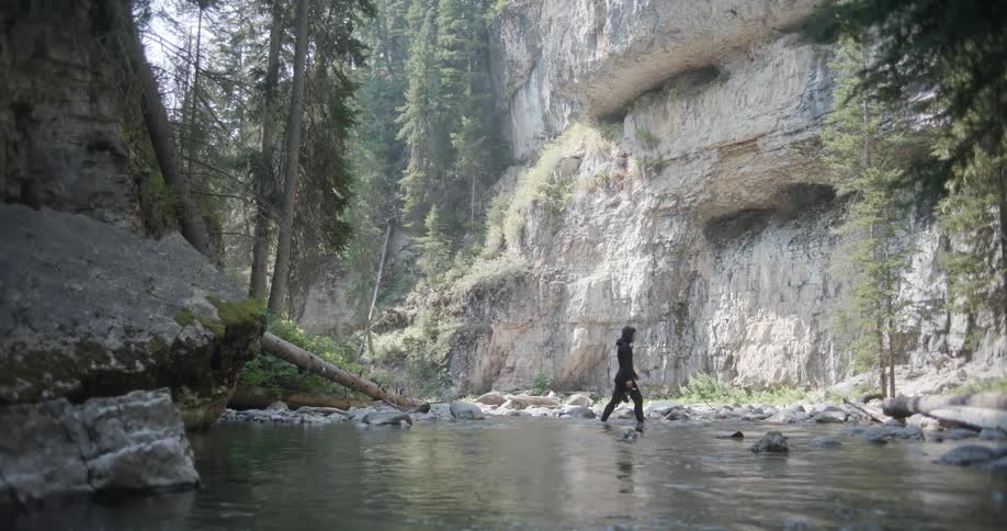 A woman wearing a wet suit and carrying a snorkel walks across a river