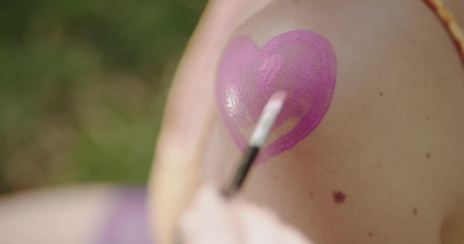 A woman paints a pink heart on a friends shoulder