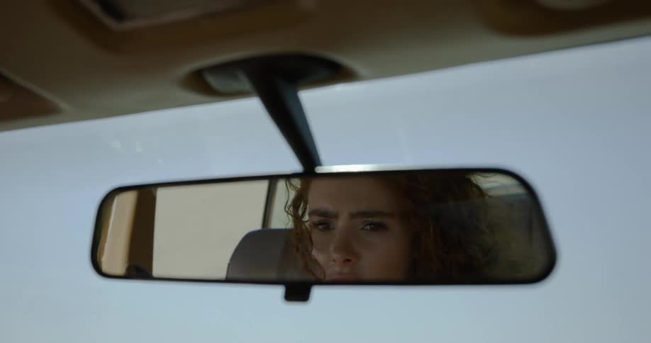 A young woman reflected in a rearview mirror while riding in a vehicle