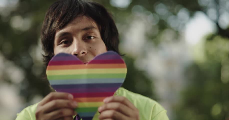 A person is holding up a colored heart outdoors in spring