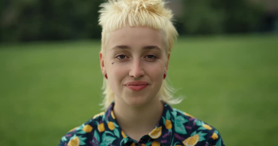 A young woman in a grassy field looks up smiles at the camera and then holds her gaze