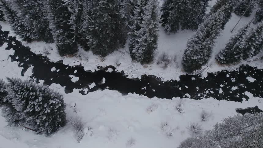 Aerial of a small river with ice chunks along a snow covered forest