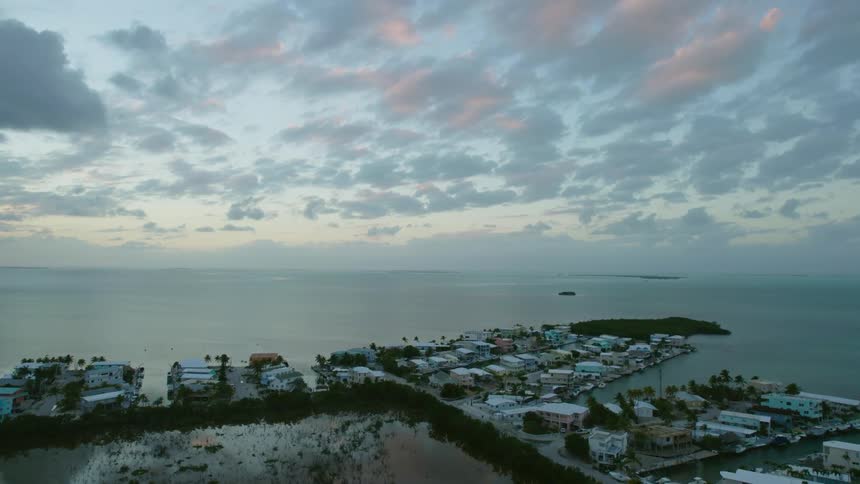 An aerial view of a coastal neighborhood with docks and boats and the horizon in the distance at dusk