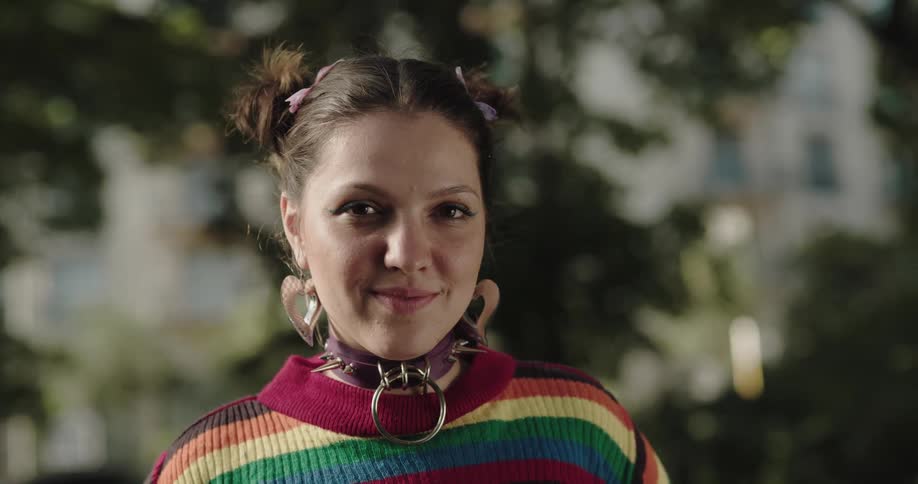 A woman with large jewelry and a rainbow sweater stares into the camera