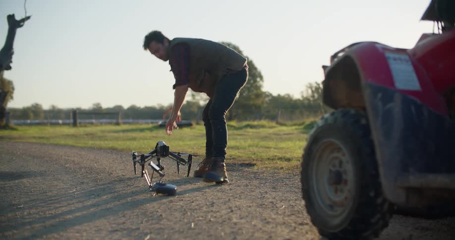 Man places drone on dirt road then picks up controller and perches on all terrain vehicle