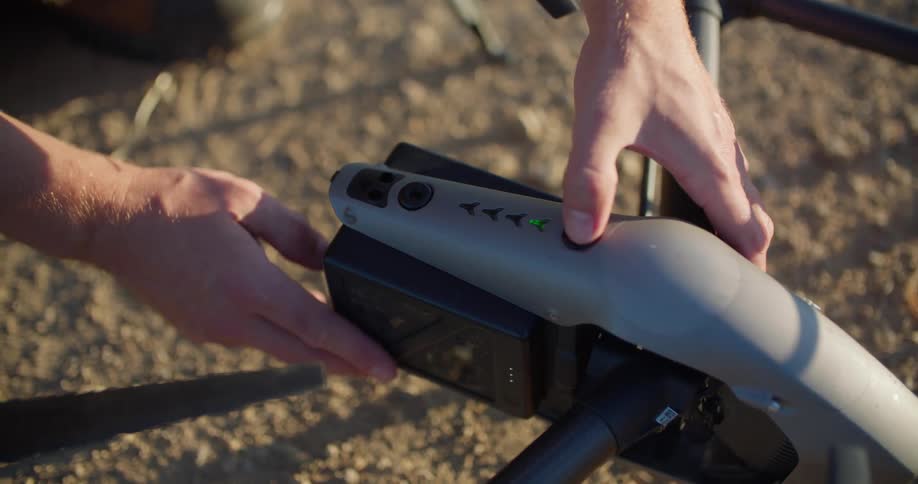 A man puts a battery in a drone sitting on the ground and turns it on