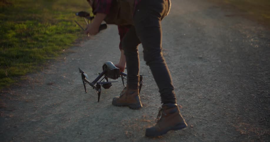 A drone is sitting on the ground and a man picks it up and walks away
