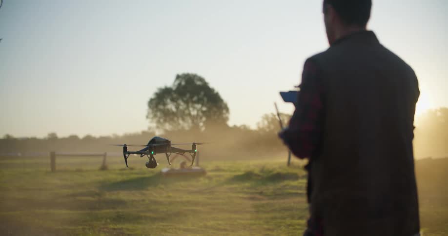 A man is holding a remote controller and operating a drone as it lifts off from the ground