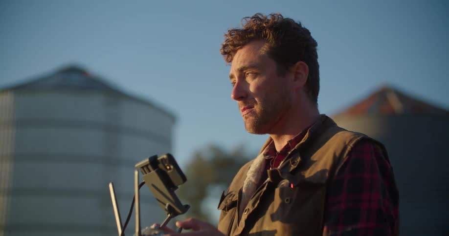 A man is standing outside holding a remote control device for a drone in both hands