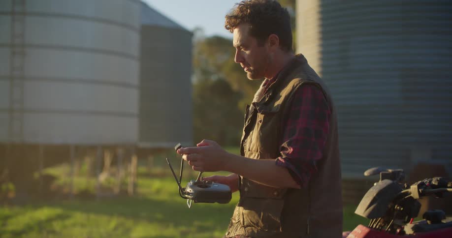 A man walks to an allterrain vehicle and turns around and he is holding a remote control device for a drone in both hands