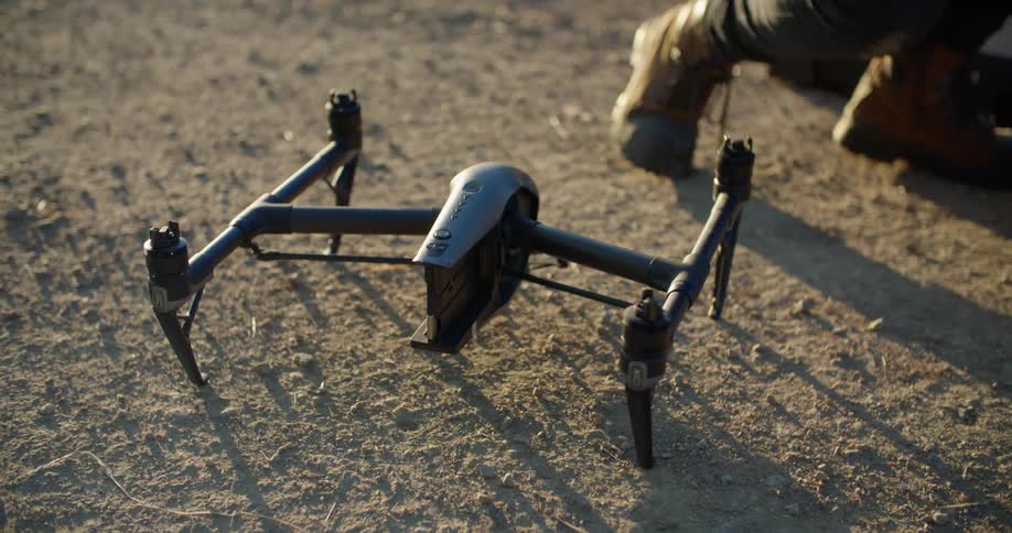 Man puts together drone while crouching on dirt road near silo