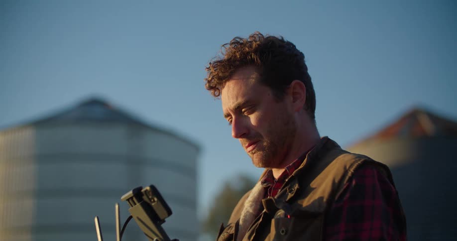 A man is standing outside holding a remote control device for a drone in both hands